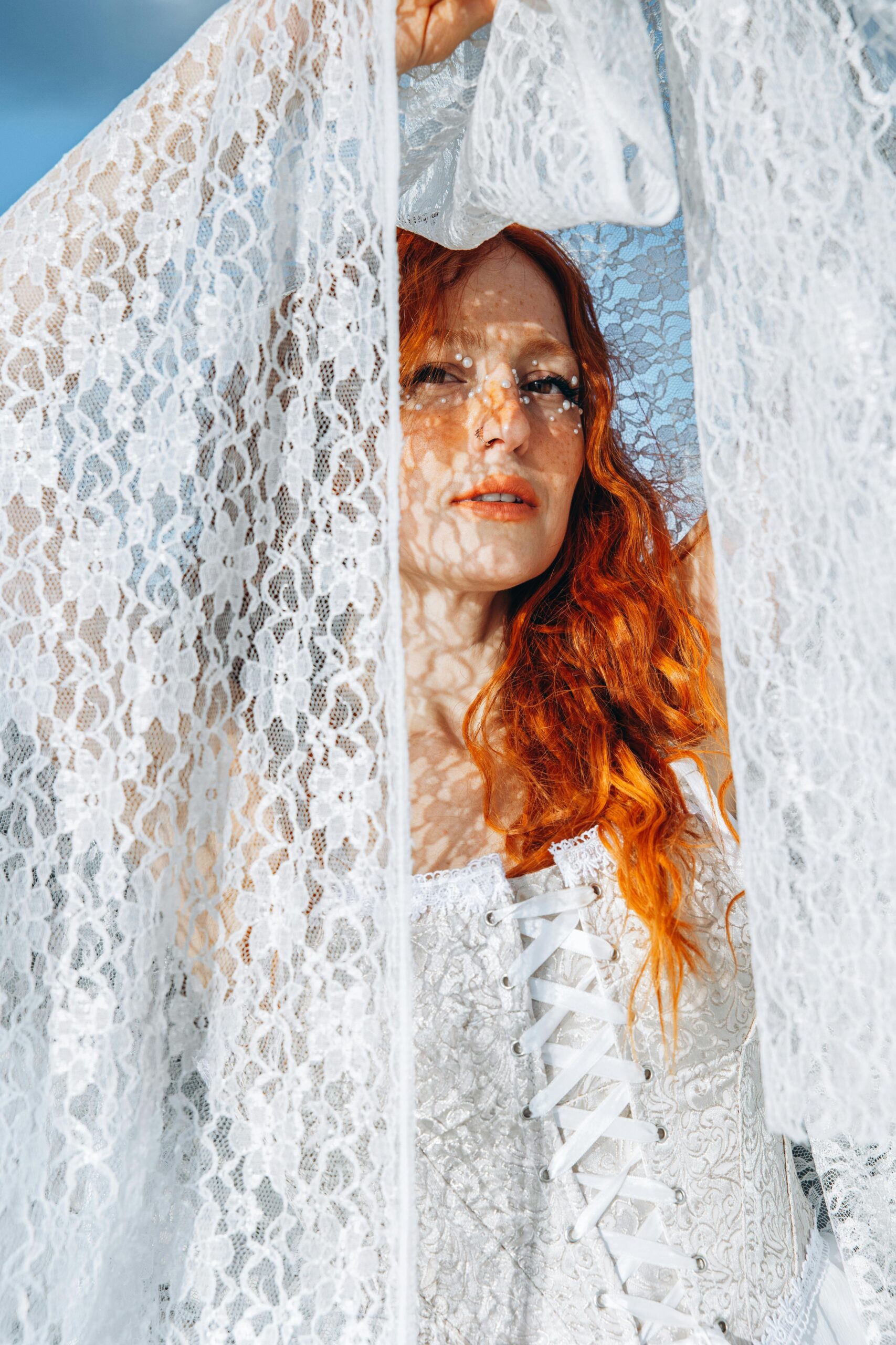 Portrait of a woman in a lace dress with red hair, casting intricate shadows outdoors.