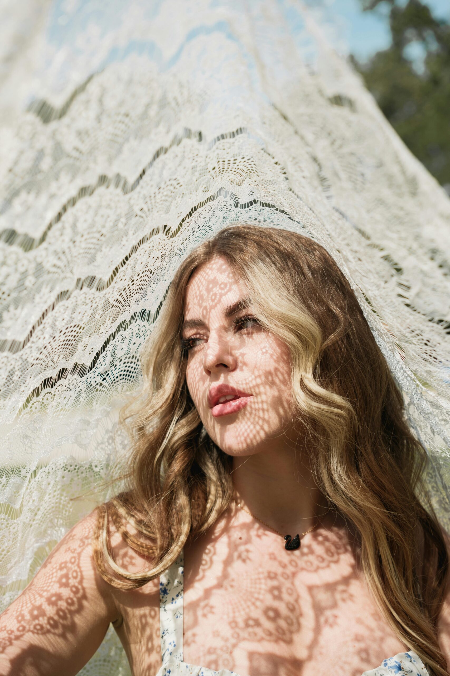 A young woman casts intricate lace shadows in a sunlit outdoor setting.