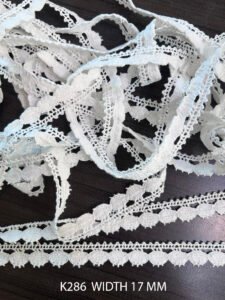 Close-up of white crochet ball lace K286, 17mm wide cotton trim with soft textured pattern for garments and decor.