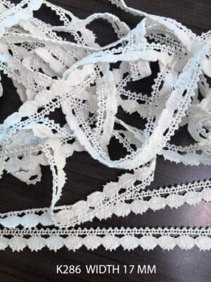 Close-up of white crochet ball lace K286, 17mm wide cotton trim with soft textured pattern for garments and decor.